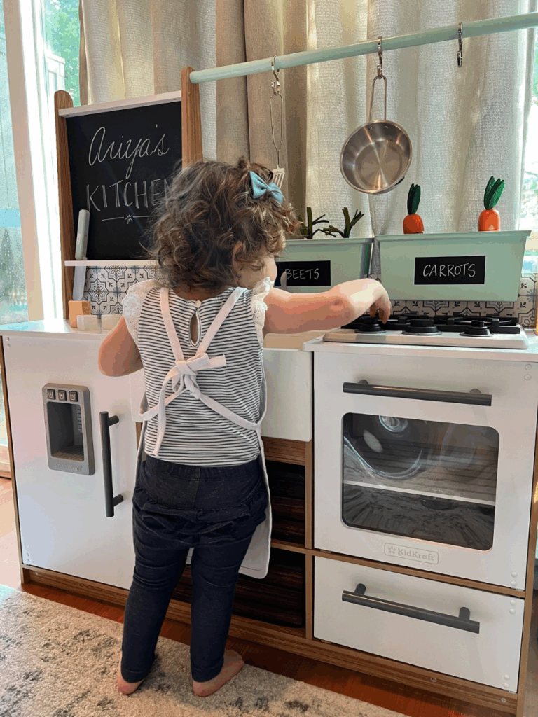 Little girl standing in front of play kitchen