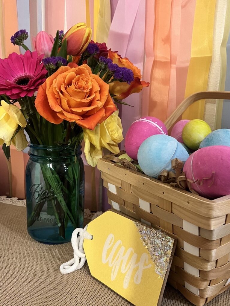 Painted paper eggs in a basket next to a Spring floral arrangement